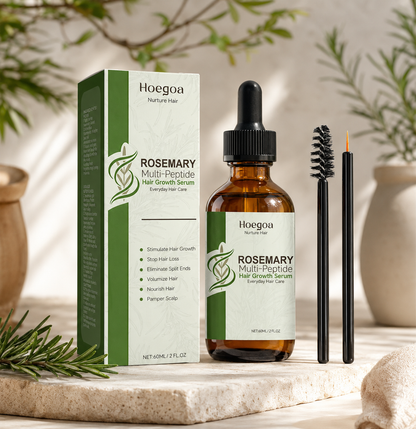 Hoegoa Rosemary Multi-Peptide Hair Growth Serum shown with its green and white box, an amber glass dropper bottle, and two black applicator tools on a stone surface with soft botanical props in the background.